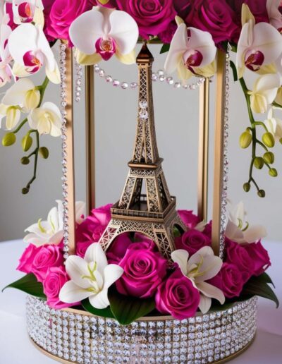 Pink Paris quinceanera theme centerpiece idea with an eiffel tower surrounded by roses on a circular base decorated with diamonds.