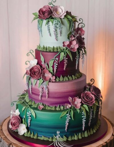 Enchanted forest quinceañera theme cake with three tiers in dark green and burgundy with burgundy roses, light pink roses and greenery, on top of a wooden circle log.