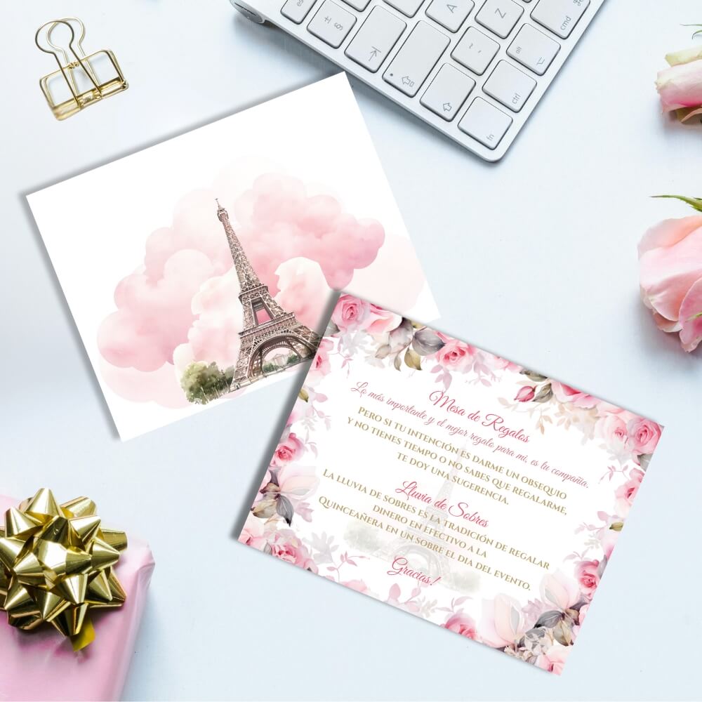 Pink paris quinceañera lluvia de sobres mockup cards showing the back featuring pink clouds and an eiffel tower, and the front of the card with floral design and eiffel tower in the background. on the left bottom there is a quinceañera gift with a gold bow, on the right are to roses, on the top is a partial view of a computer keyboard.